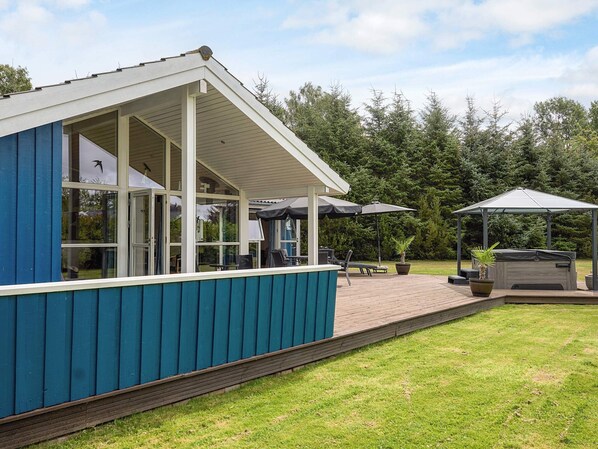 Un espacio de estar al aire libre cubierto con mesas y sombrillas, un jacuzzi y una terraza de madera.