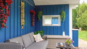 A covered outdoor seating area with a sofa and a table, surrounded by blue walls and various plants. - 4 Star Holiday Home in Nexo (Nexø)