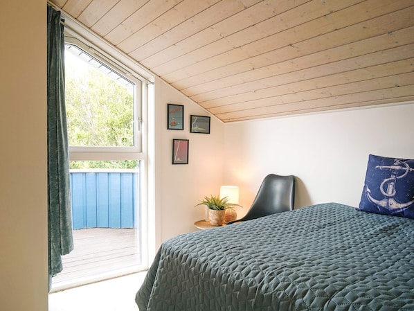 A bedroom with a bed, a chair, a lamp, and a window with curtains.