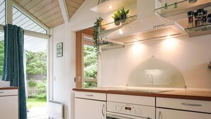 A modern kitchen with a built-in oven, a glass-top island, and a view of the garden through the window. - 4 Star Holiday Home in Nexo (Nexø)