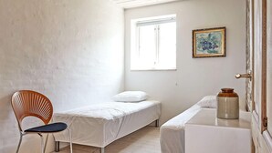 A small, sparsely furnished room with two single beds, a wooden chair, a small table, and a window.
