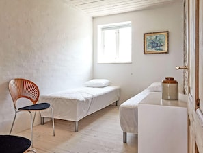 Une petite pièce, peu meublée, avec deux lits simples, une chaise en bois, une petite table et une fenêtre.