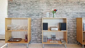 Two wooden display shelves against a brick wall, one with glassware and the other with audio equipment and CDs.