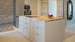 A modern kitchen with a central island, built-in appliances, and a rustic brick wall.