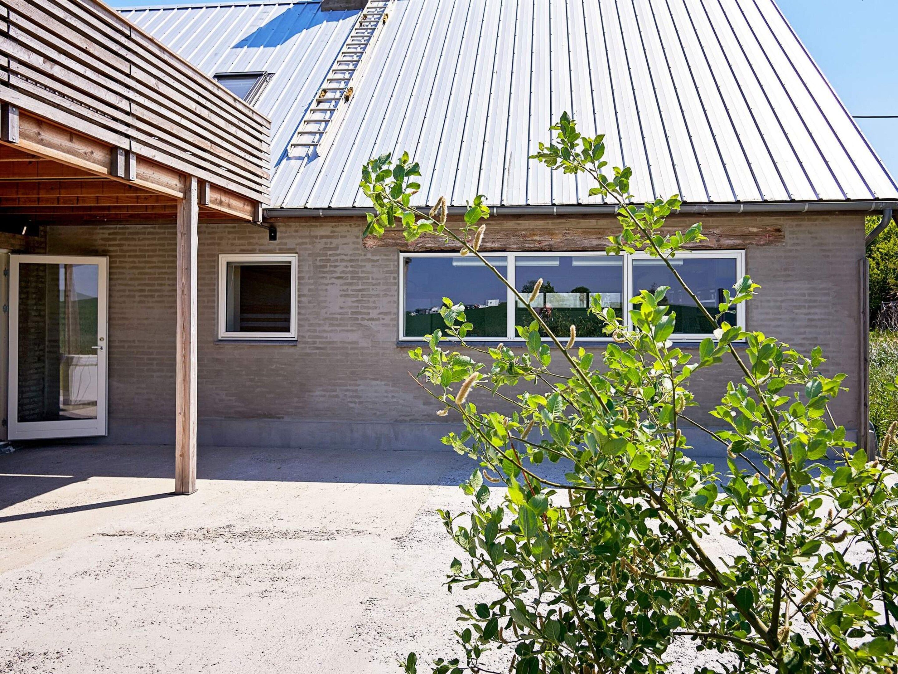 A building with a metal roof, a wooden structure to the left, and a window with a view of the sky.