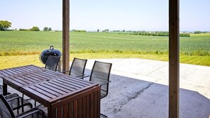A covered outdoor area with a table and chairs, a barbecue grill, and a view of a green field. - 5 Star Holiday Home in Svaneke (Svaneke)