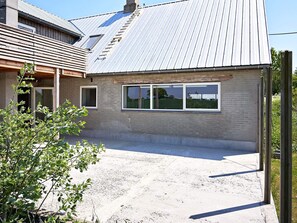 Un bâtiment à deux étages, doté d’un toit en métal, d’une allée en béton et d’un petit jardin agrémenté d’arbustes.