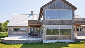 A modern two-story house with a large window and a patio with outdoor furniture. - 5 Star Holiday Home in Svaneke (Svaneke)