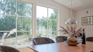 A dining area with a wooden table, six grey upholstered chairs, a hanging pendant light, a vase with dried plants, and a wine bottle. - 6 Person Holiday Home in Aakirkeby (Akirkeby)