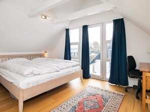 A bedroom with a wooden bed, a desk with a chair, a patterned rug, and a view through a large window with curtains. - 5 Person Holiday Home in Otterup (Otterup)