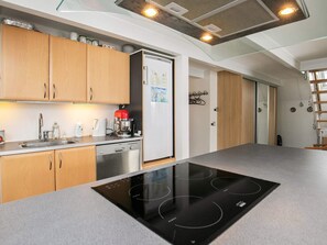 A modern kitchen with wooden cabinets, a built-in dishwasher, a black induction cooktop, and a refrigerator with children's drawings on it. - 5 Person Holiday Home in Otterup (Otterup)