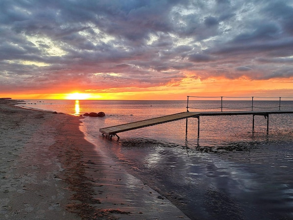 A sunset over a beach with a wooden pier and rocky outcrops.