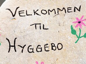 A stone with 'VELKOMMEN TIL HYGGEBO' written on it, accompanied by a pink flower drawing. - 5 Person Holiday Home in Otterup (Otterup)