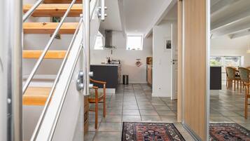 A modern interior with a staircase, kitchen, dining area, and a view of the outdoors.