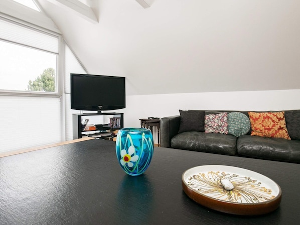 A living room with a black leather sofa, a television on a stand, and a decorative glass vase on a table.
