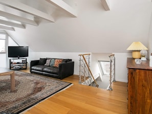 A modern living room with a black leather sofa, a flat-screen TV, a wooden coffee table, and a patterned rug.