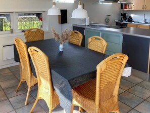 A modern kitchen with a dining area, featuring a large table, wicker chairs, and pendant lighting. - 5 Person Holiday Home in Otterup (Otterup)