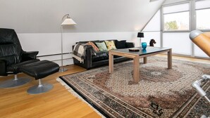 A modern living room with a black leather chair, a black sofa, a wooden coffee table, and a patterned rug. - 5 Person Holiday Home in Otterup (Otterup)