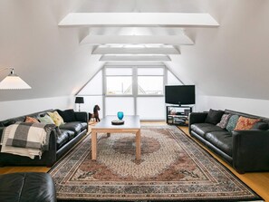 A modern living room with a high ceiling, two leather sofas, a coffee table, a TV, and a large window. - 5 Person Holiday Home in Otterup (Otterup)