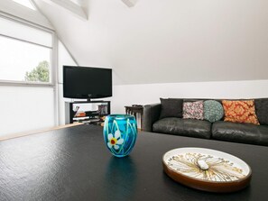 A living room with a black leather sofa, a television on a stand, and a table with a decorative plate and a glass vase. - 5 Person Holiday Home in Otterup (Otterup)