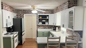 A kitchen with white cabinets, a black refrigerator, a wooden dining table with chairs, and a brick-patterned backsplash.