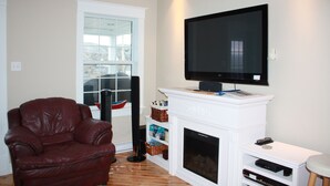 Un salon avec un canapé en cuir, une cheminée, un téléviseur fixé au mur et une fenêtre donnant sur un beau paysage.
