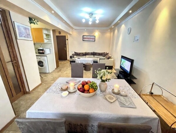 A dining area with a table set for two, a television, and a sofa in the background.