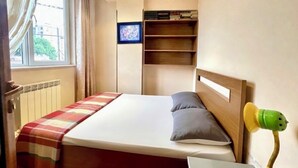 Makuuhuone, jossa on sänky, hylly, ikkuna ja seinälle asennettu televisio.