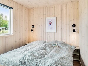 A bedroom with a bed, a window, wooden walls, and two wall-mounted lamps. - 5 Star Holiday Home in Vejby (Vejby)