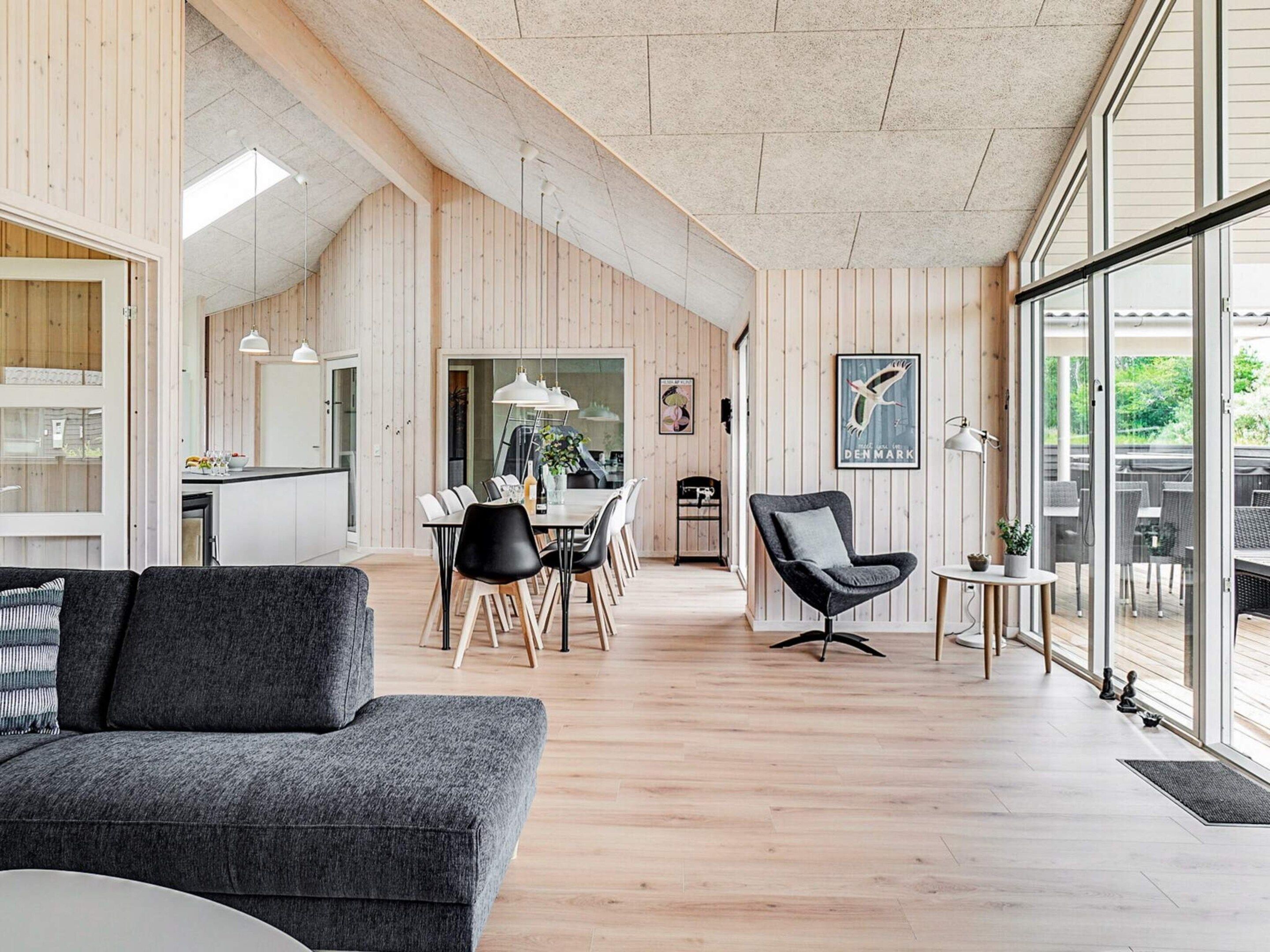 A modern interior with a dining area, a sofa, and a view through large windows.