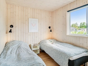 A room with two beds, wooden walls, a window with a view, and a framed picture on the wall. - 5 Star Holiday Home in Vejby (Vejby)