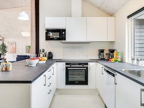 A modern kitchen with white cabinets, a black microwave, a built-in oven, and a stainless steel sink. - 5 Star Holiday Home in Vejby (Vejby)
