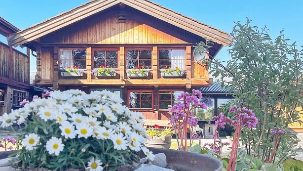 A wooden chalet with a balcony, surrounded by flowers and plants. - 5 Person Holiday Home in Ringebu (Ringebu)