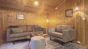 A cozy room with wooden walls, a sofa, a chair, and a round ottoman. - 5 Person Holiday Home in Ringebu (Ringebu)
