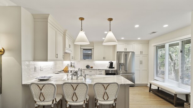 A modern kitchen with white cabinetry, a central island with bar stools, a stainless steel refrigerator, and pendant lighting.