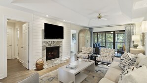 A spacious living room with a fireplace, comfortable seating, and a large window offering a view of the outdoors.