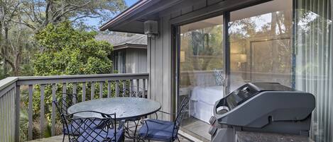 Una terrassa amb taula i cadires, una barbacoa i una porta corredissa de vidre que dóna a un dormitori.