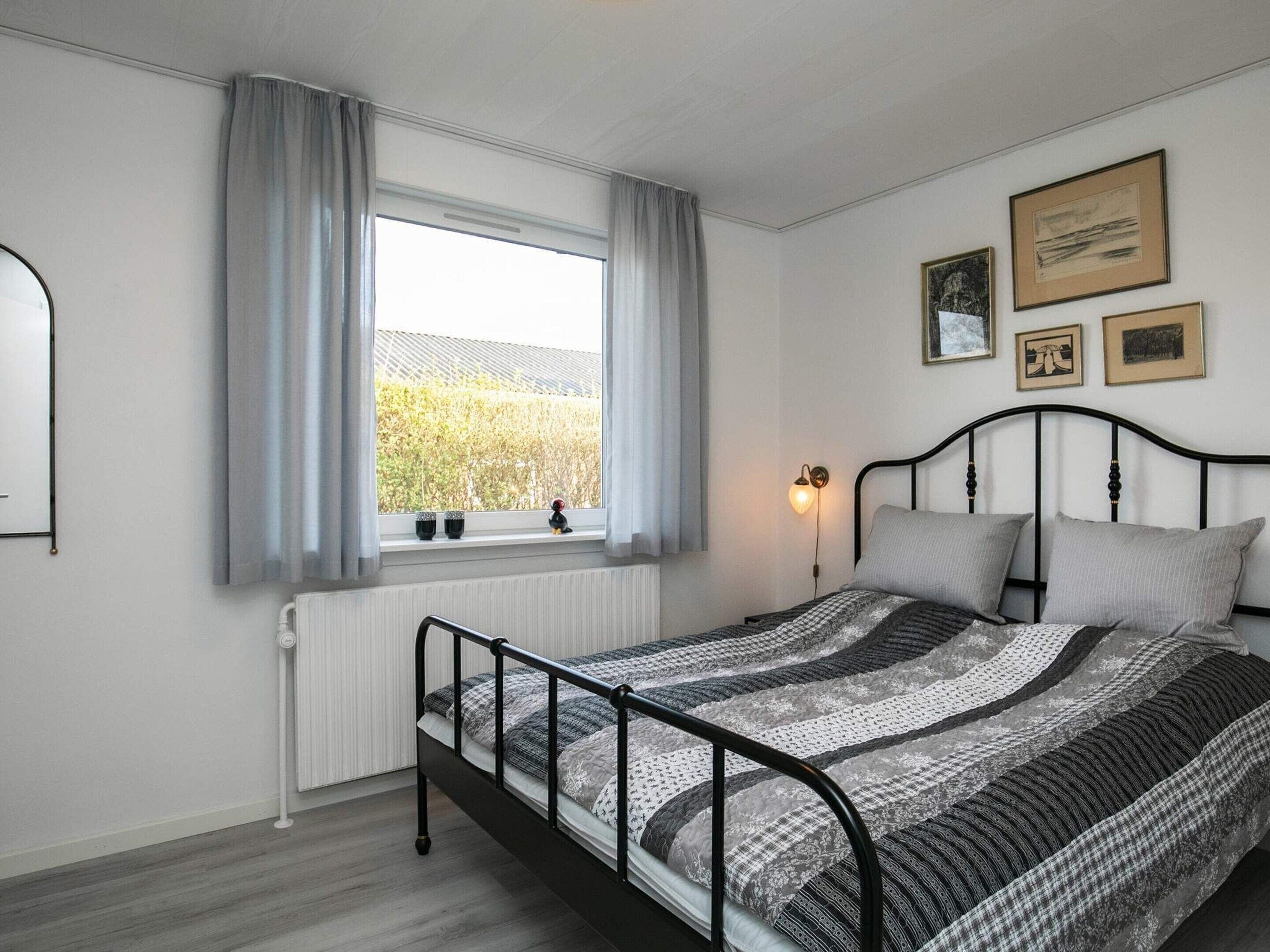 A bedroom with a bed, a window with curtains, a radiator, and wall-mounted pictures.