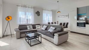 A modern living room with a sectional sofa, a coffee table, and a kitchen area with appliances. - Holiday apartment with shared pool (Medulin)