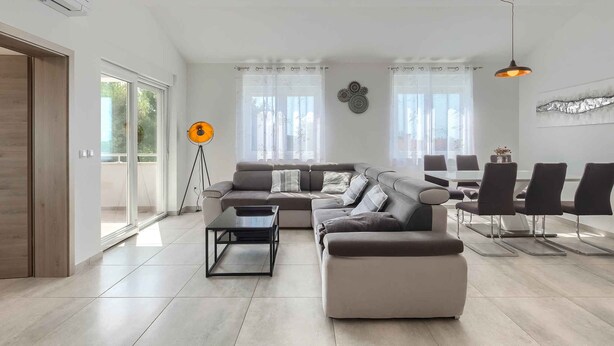 A modern living room with a sectional sofa, a coffee table, and a dining area with chairs. - Holiday apartment with shared pool (Medulin)