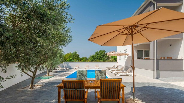 An outdoor pool area with lounge chairs and a table, surrounded by a white building.