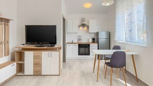 A modern kitchen with a TV, cabinets, a stove, and a dining area with chairs.