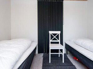 A room with two single beds, a white chair, and a black curtain.