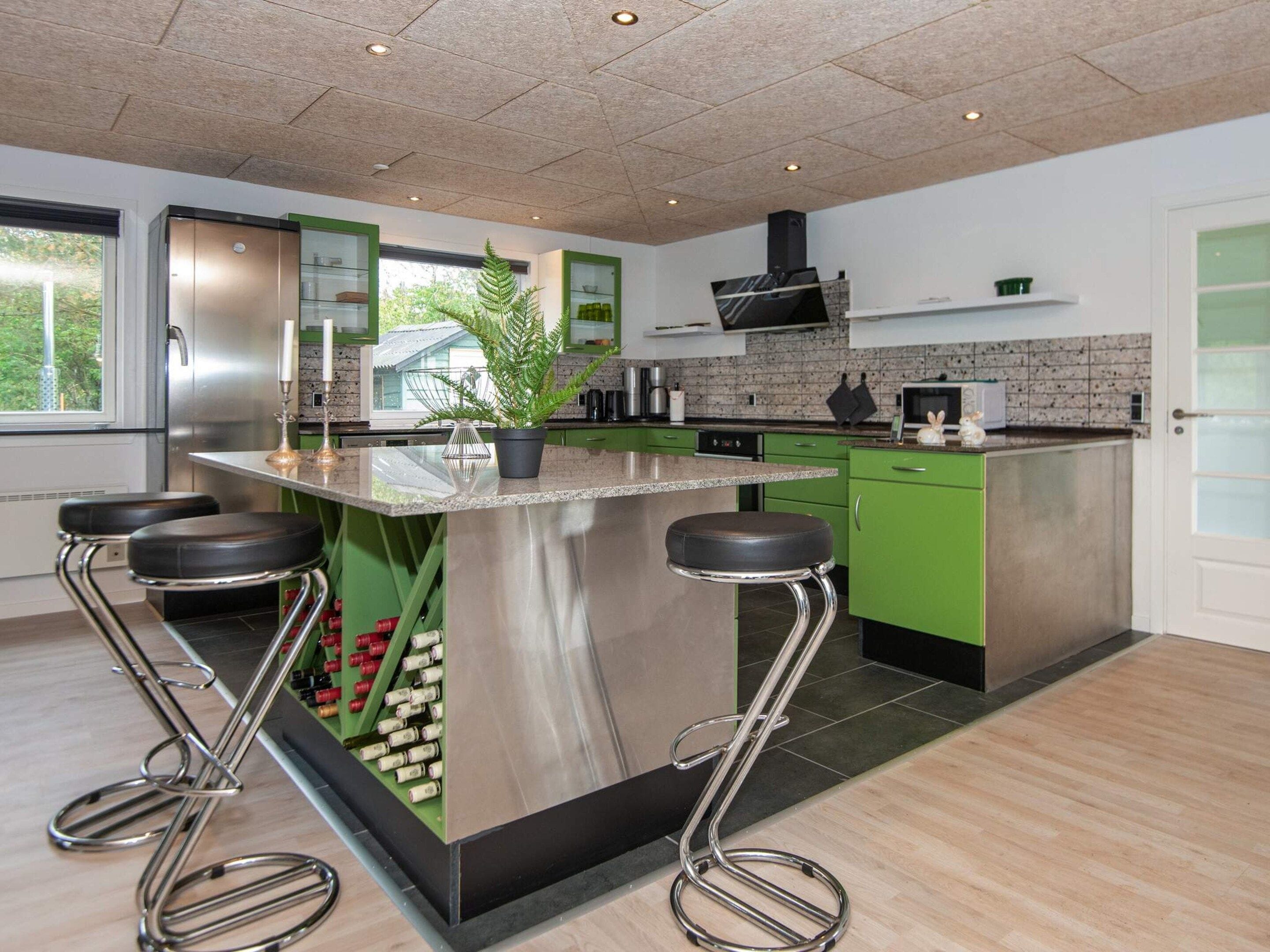 Une cuisine moderne dotée d’un îlot central, de meubles verts, d’appareils électroménagers en acier inoxydable et d’une grande fenêtre.