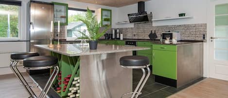 A modern kitchen with a central island, green cabinets, stainless steel appliances, and a large window.