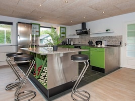 Uma cozinha moderna com ilha central, armários verdes, eletrodomésticos de aço inoxidável e uma grande janela.
