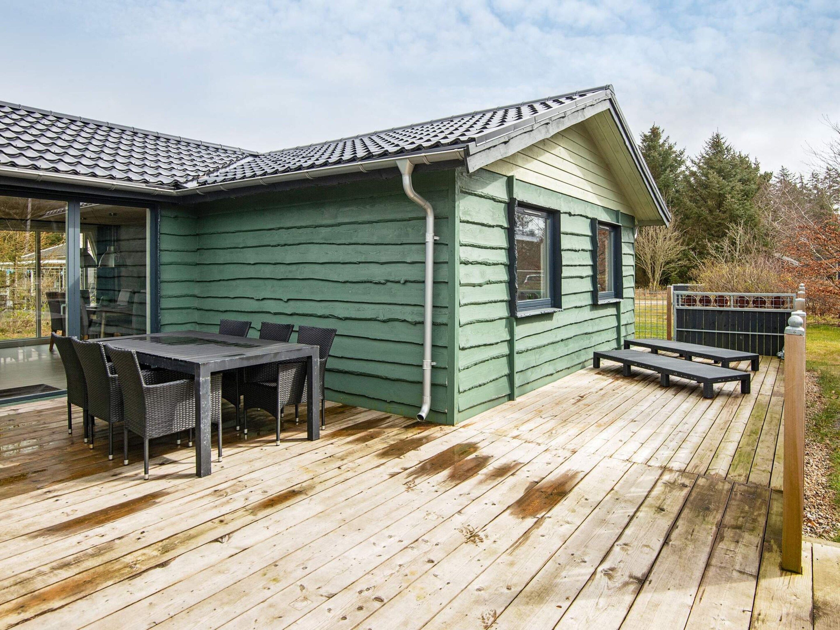 A wooden deck with a dining table and chairs, a covered patio area, and a view of the surrounding landscape.
