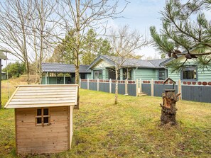 A row of wooden cabins with a fenced yard, a small wooden shed, and a tree stump with a birdhouse. - 4 Star Holiday Home in Hemmet (Hemmet)