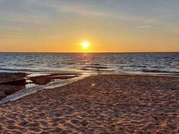 A beach with the sun setting over the ocean, waves gently lapping at the shore.