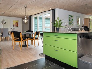 A modern kitchen with green cabinetry, a stainless steel dishwasher, and a dining area with wooden chairs and a table.
